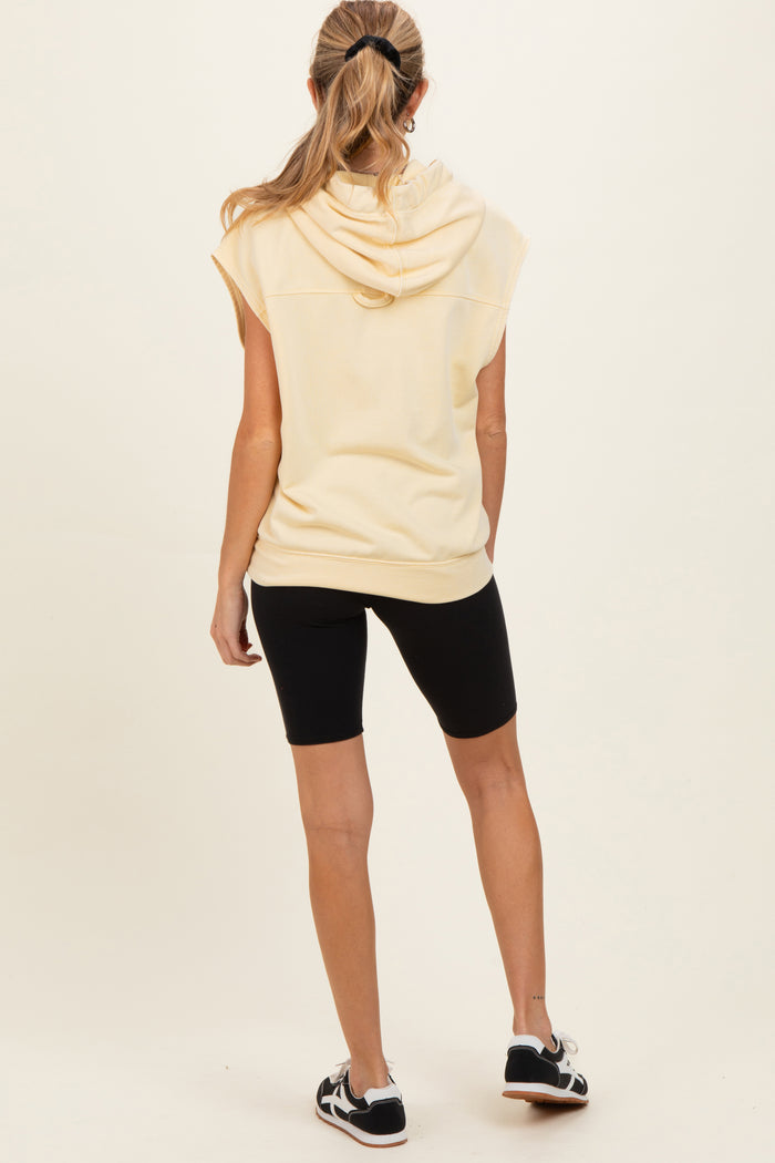 woman wearing a yellow sleeveless maternity hoodie and black bike shorts, with her back facing the camera