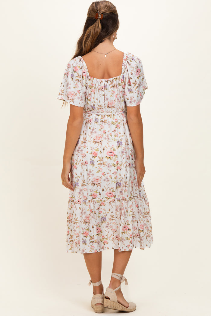 woman wearing a floral midi maternity dress with short puff sleeves and a smocked bodice, showing a baby bump