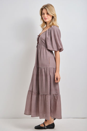 woman wearing a brown checkered maxi dress with puff sleeves and a tiered skirt, standing sideways