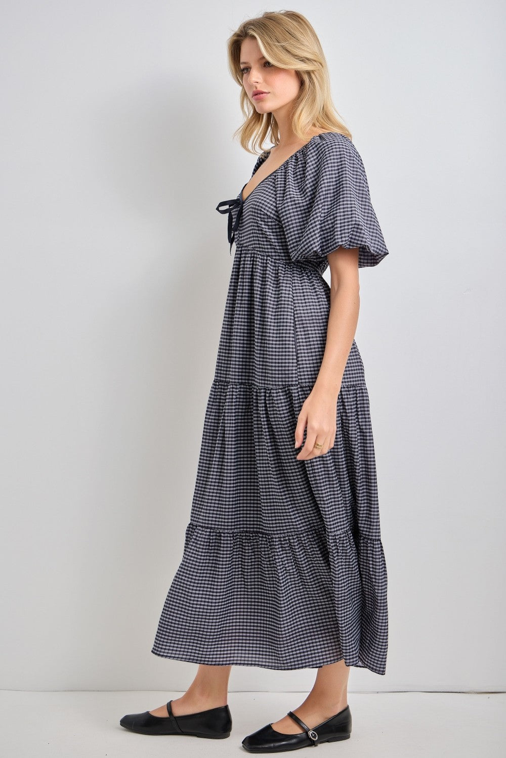 woman wearing a navy and white checkered tiered maxi dress with short sleeves and a front tie detail