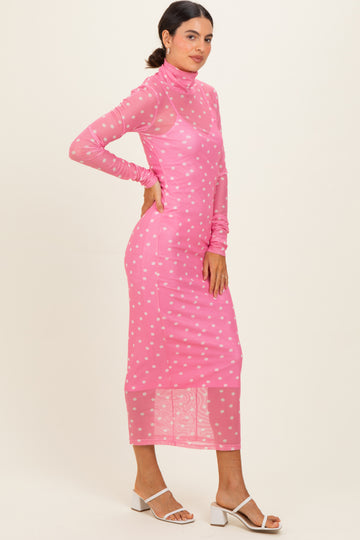 woman wearing a pink long sleeve midi dress with white polka dots and a high neck, styled with white block-heeled sandals