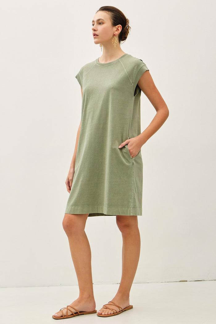 woman wearing a green short sleeve dress with pockets and relaxed fit, standing confidently with neutral sandals.