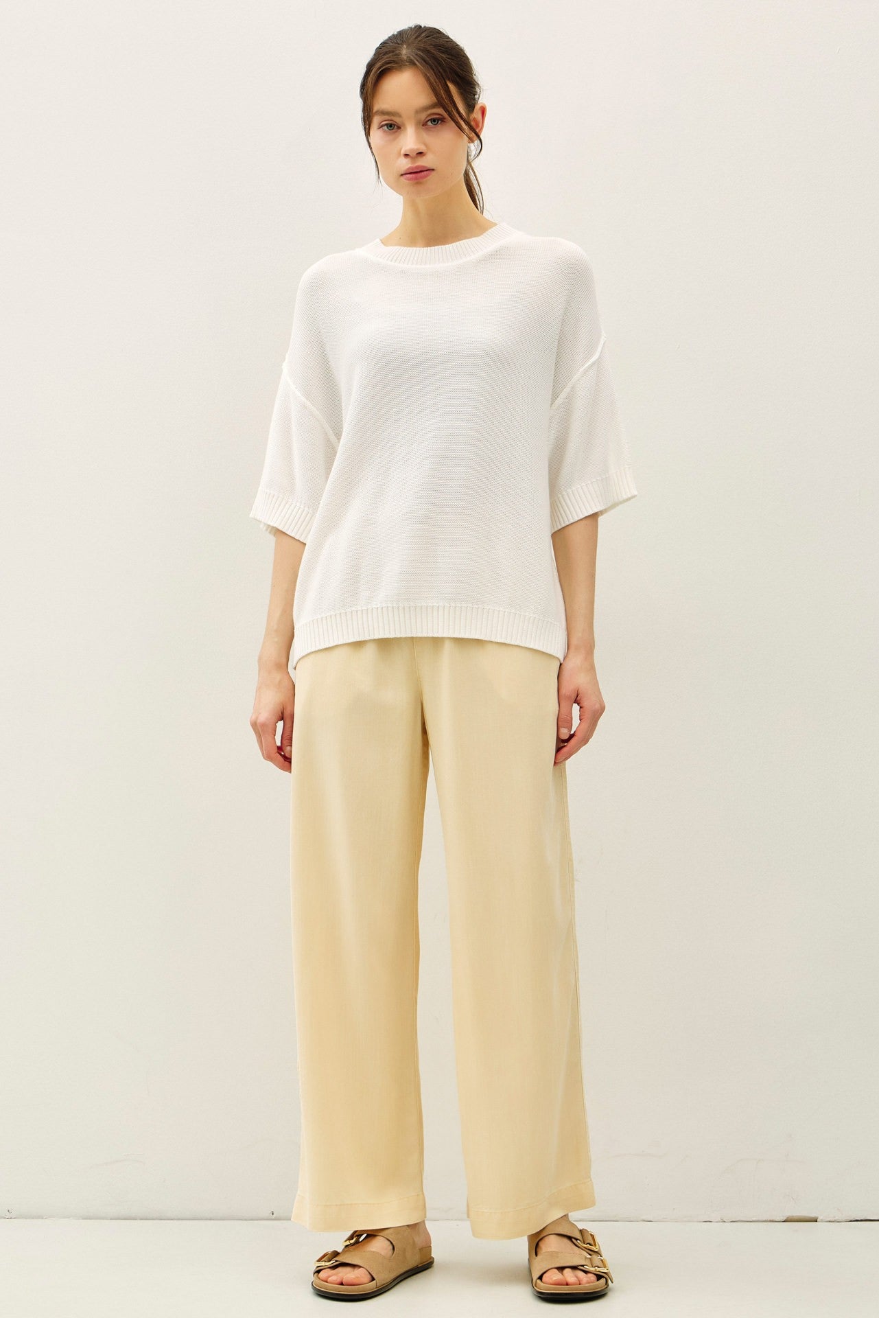 woman wearing a white oversized knit sweater paired with wide-leg beige trousers