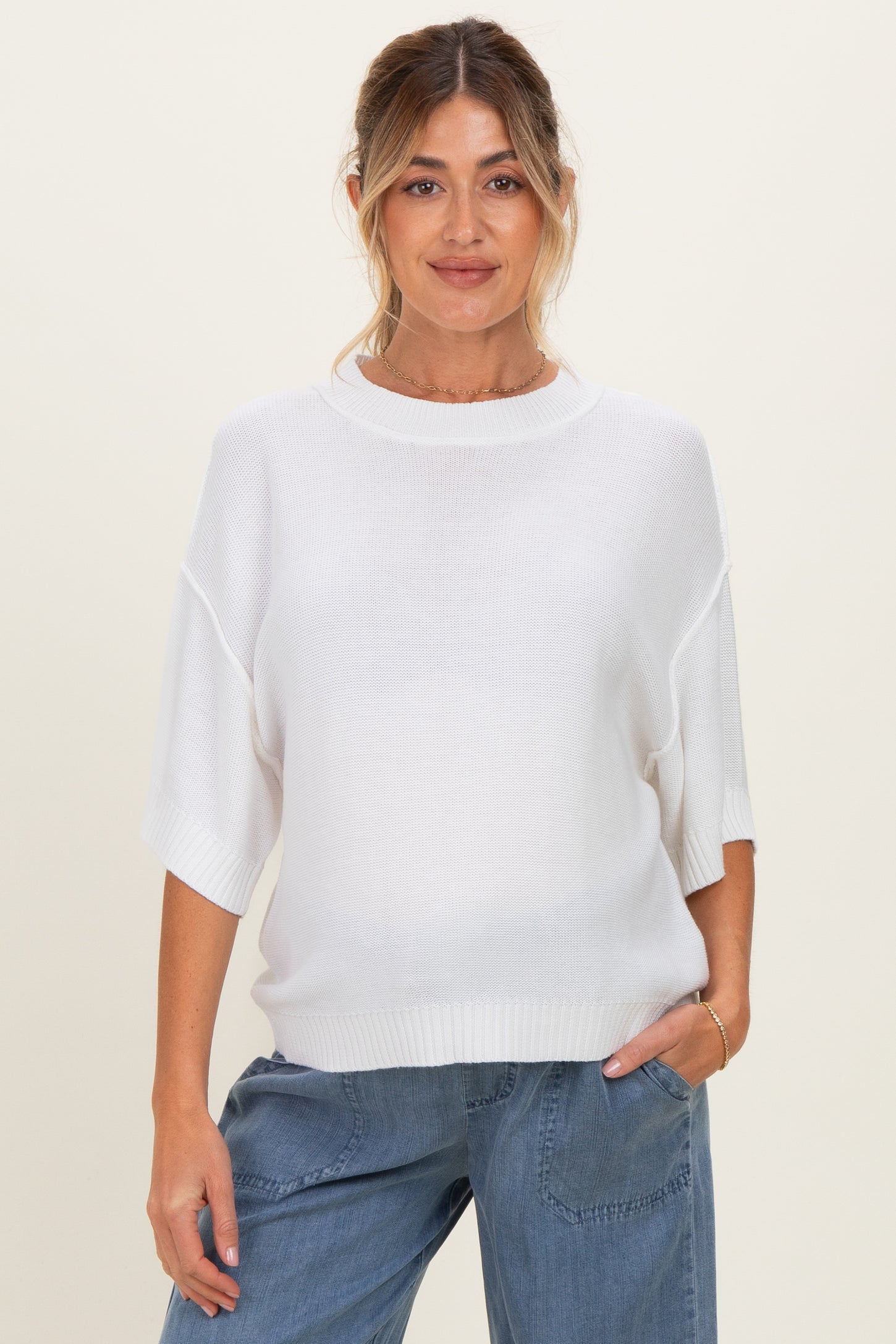 woman wearing a white short sleeve maternity sweater with relaxed fit and a visible baby bump