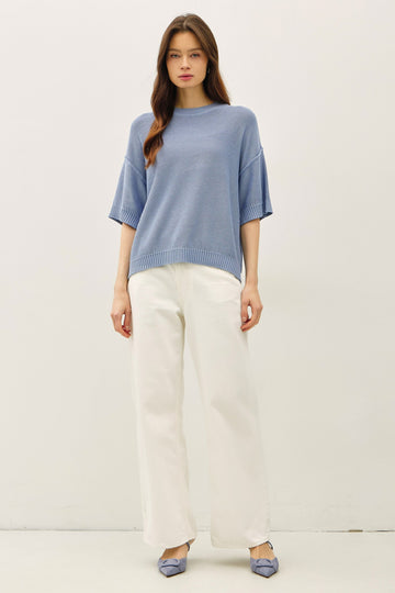 woman wearing a light blue oversized knit sweater and cream wide-leg pants, paired with blue flat shoes