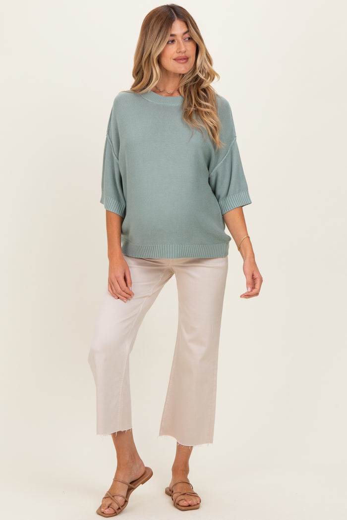 woman wearing a light green oversized knit maternity sweater and cream wide-leg pants, showing her baby bump