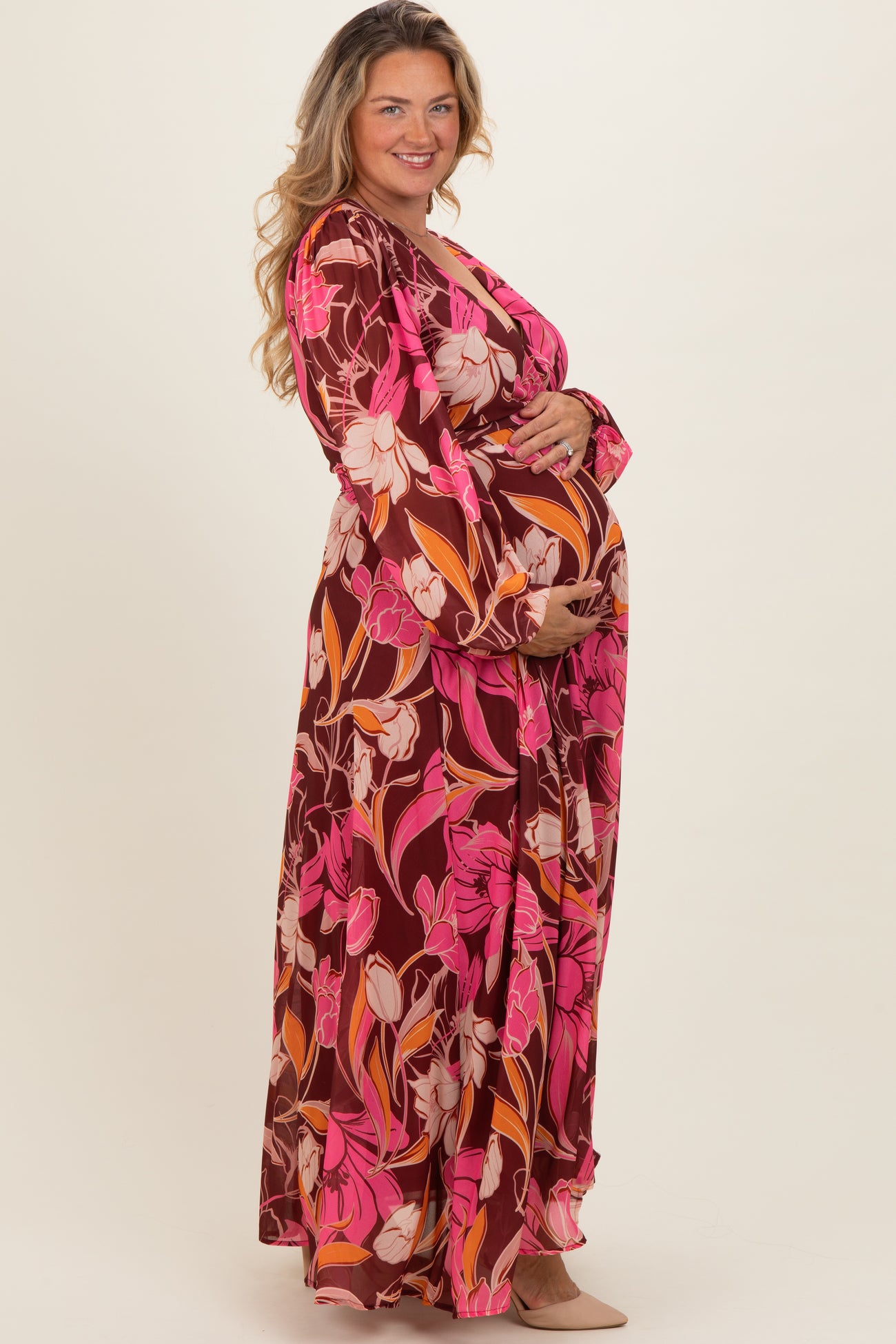woman wearing a vibrant floral print maternity maxi dress and holding her baby bump