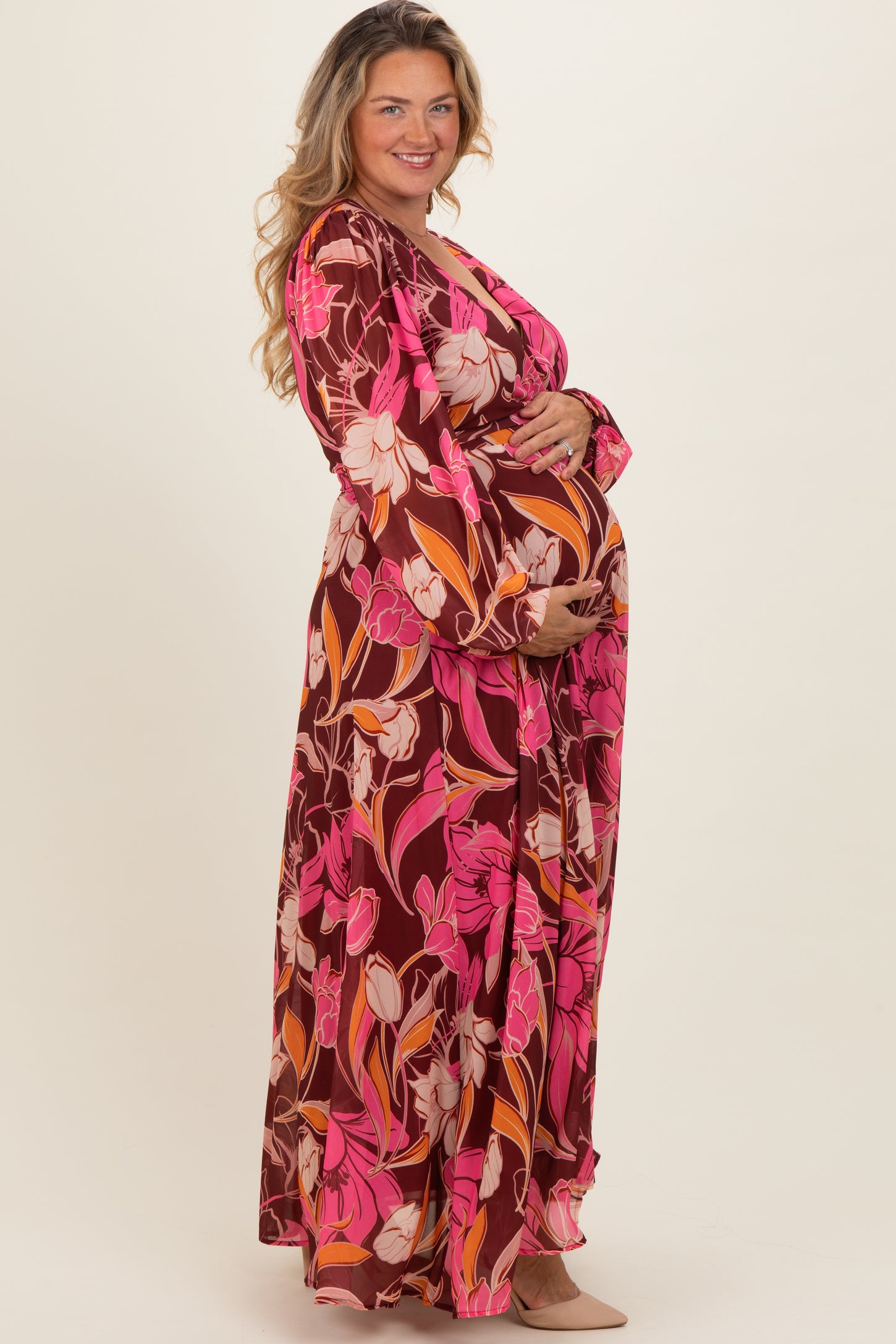 woman wearing a vibrant floral print maternity maxi dress and holding her baby bump