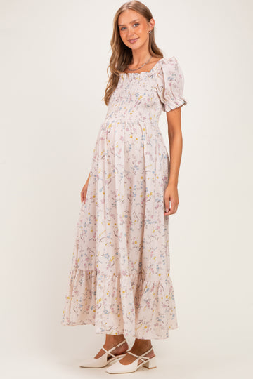 woman wearing a light pink floral maternity dress with short puff sleeves and a flowing maxi skirt, showing her baby bump