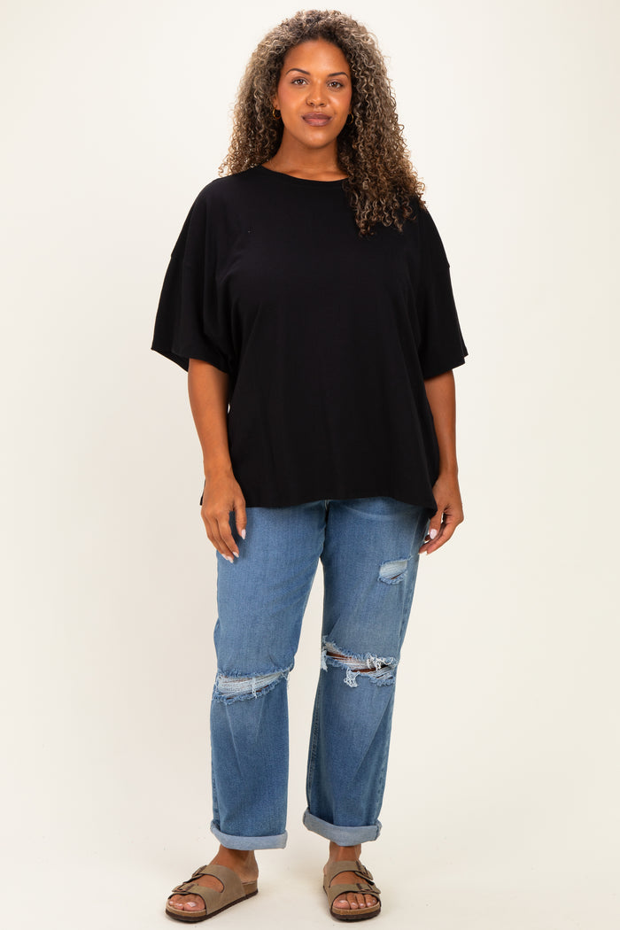 woman wearing a black oversized t-shirt and distressed blue jeans, standing against a neutral background