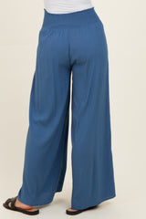 woman wearing a pair of blue wide-leg trousers with a smocked waistband and black sandals, viewed from the back