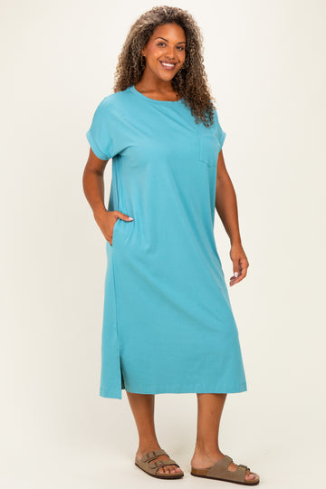 woman wearing a teal plus-size midi dress with short sleeves and side pockets, standing with a smile