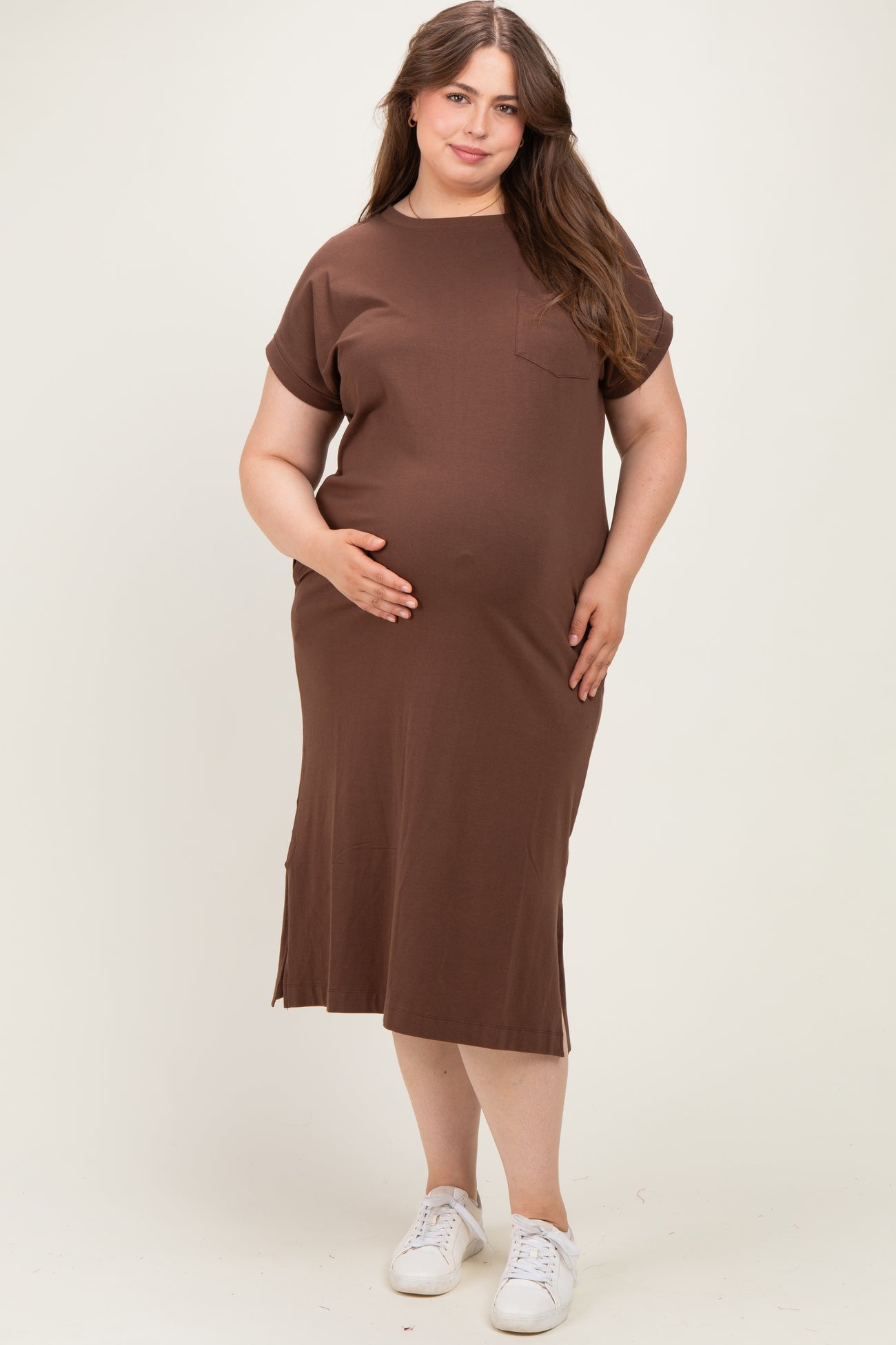 woman wearing a brown short sleeve maternity dress with a pocket and side slits, cradling her baby bump