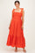 woman wearing a bright orange maternity dress with eyelet details, tiered skirt, and bow straps, showing her baby bump