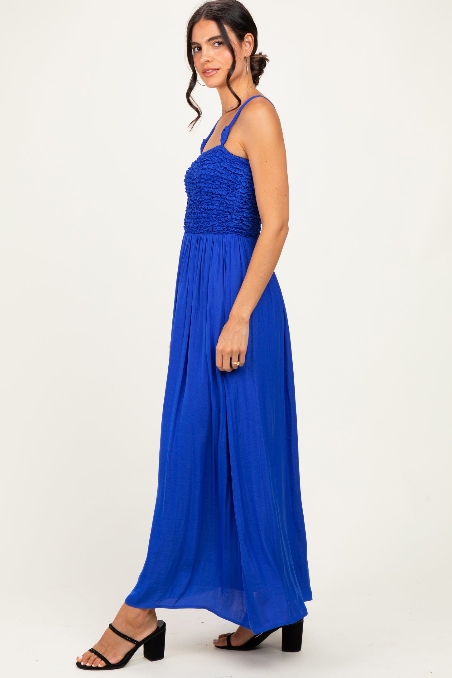 woman wearing a bright blue maxi dress with a smocked bodice and thin straps, standing sideways with black block heels