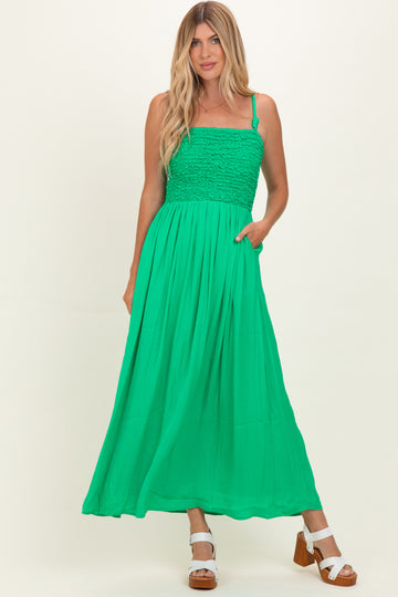 woman wearing a bright green maxi dress with a smocked bodice and adjustable straps, posing with hands in pockets