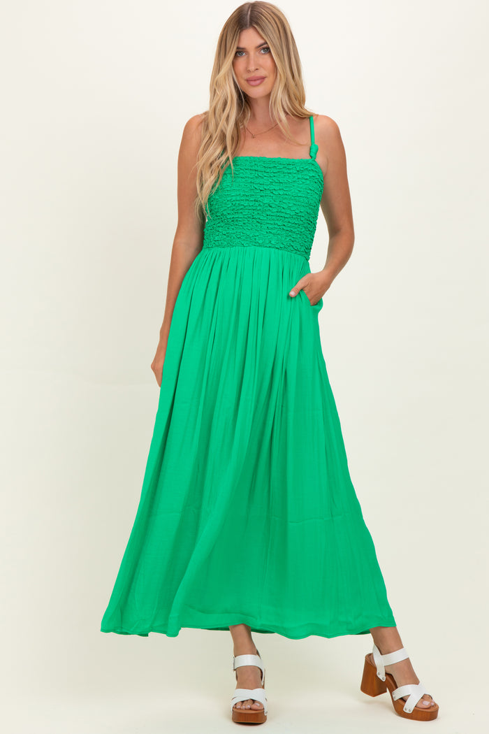 woman wearing a bright green maxi dress with a smocked bodice and adjustable straps, posing with hands in pockets