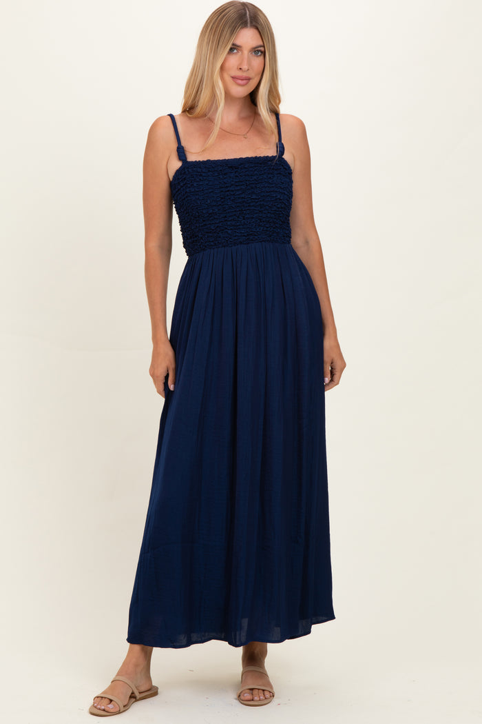 woman wearing a navy blue maxi dress with smocked bodice and spaghetti straps, standing against a light background