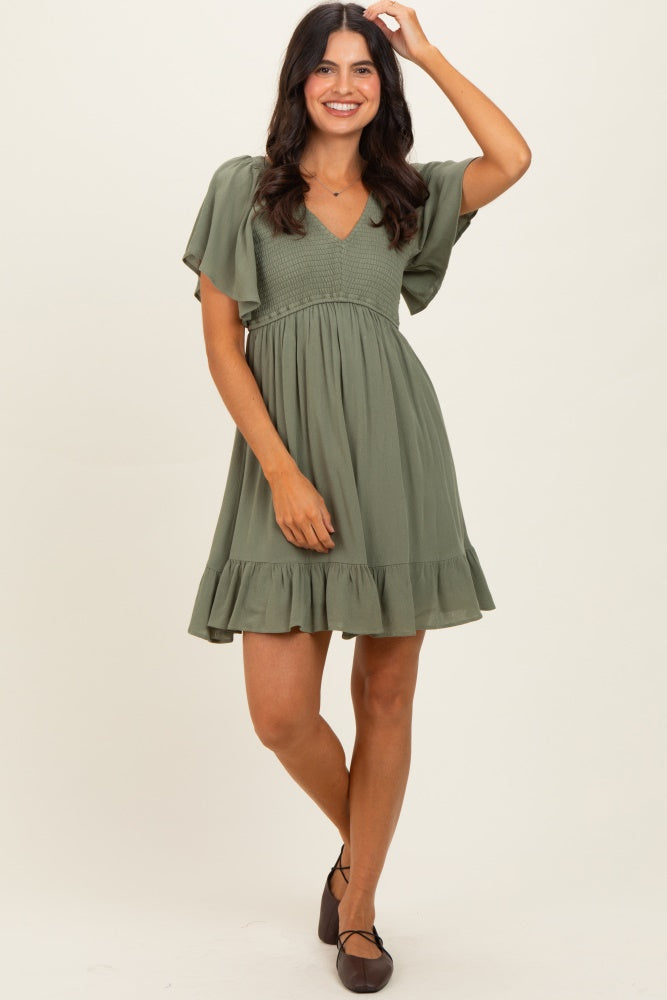 woman wearing a sage green short dress with flutter sleeves and a ruffled hem, smiling and posing