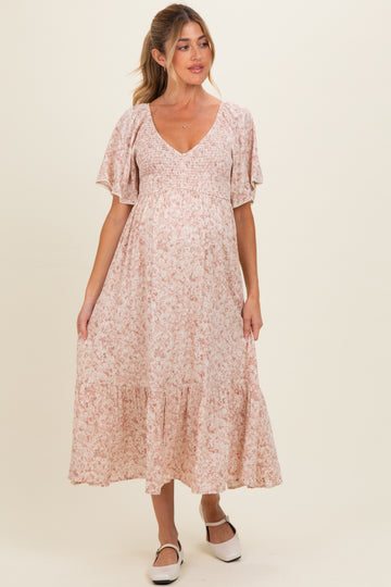 woman wearing a floral pink maternity maxi dress with short flutter sleeves and a tiered hem, showing her baby bump
