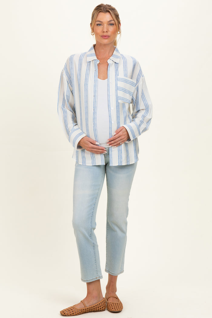 woman wearing a white and blue striped maternity shirt and light wash jeans, gently cradling her baby bump