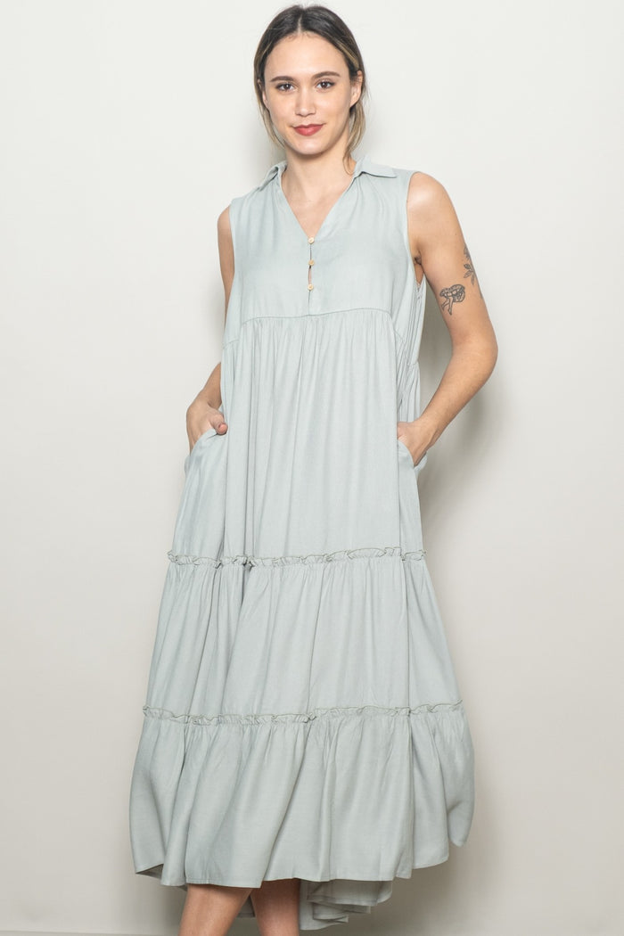 woman wearing a light green sleeveless tiered midi dress with a collared neck and side pockets