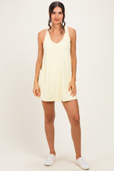 woman wearing a light yellow sleeveless dress with pockets and white sneakers