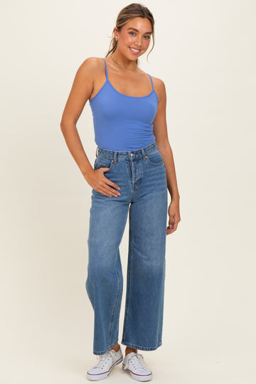 woman wearing a light blue tank top and high-waisted wide-leg jeans, posing with one hand on her hip