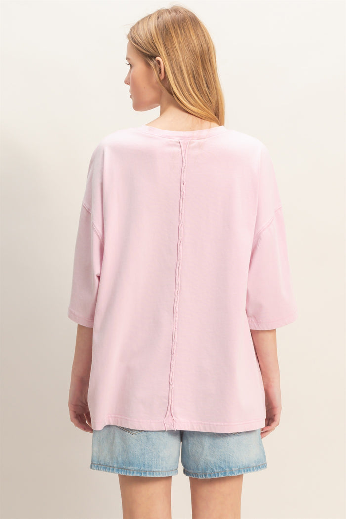 woman wearing a light pink oversized t-shirt with a back seam detail, paired with denim shorts