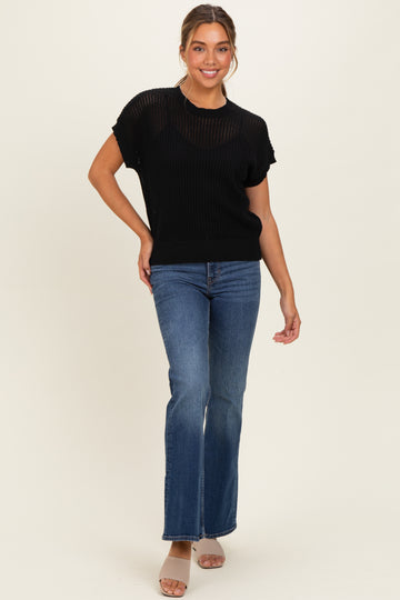 woman wearing a black short sleeve knit top and blue flared jeans, posing with one hand on her hip