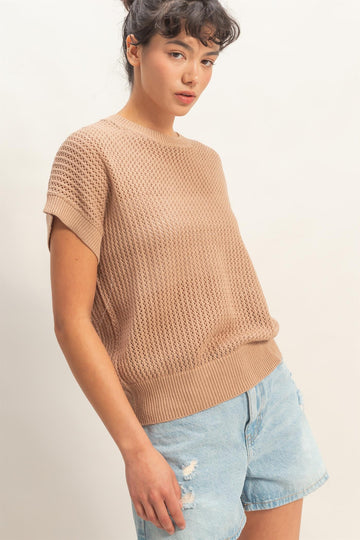 woman wearing a beige knit short sleeve sweater with a relaxed fit and paired with light blue distressed denim shorts