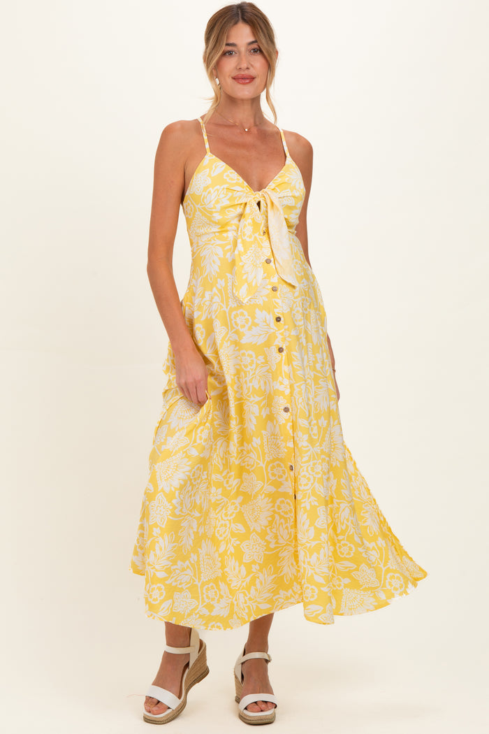 woman wearing a yellow floral maternity dress with a tie front and buttons, showcasing her baby bump