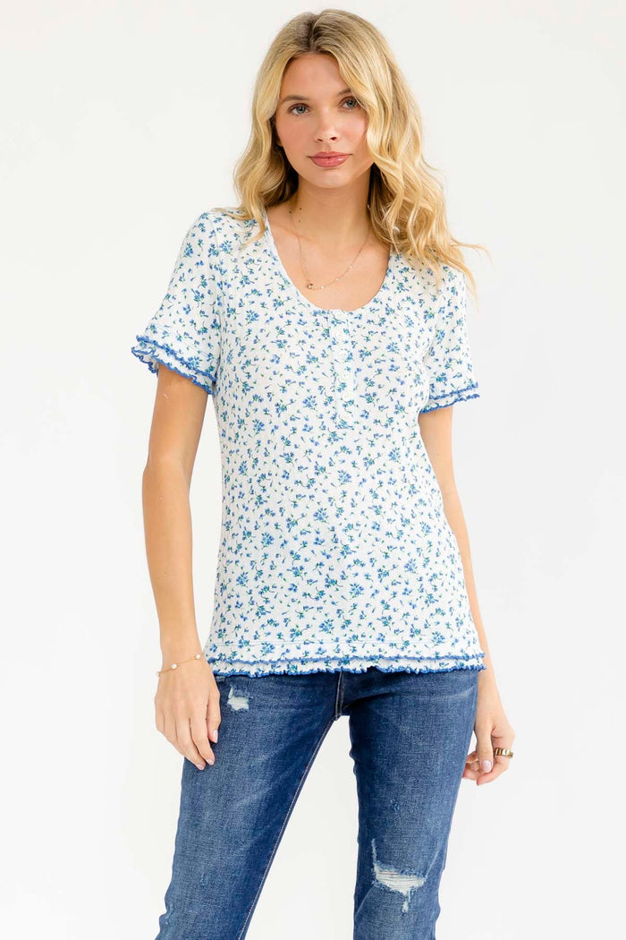 woman wearing a white floral print top with blue trim and short sleeves, paired with denim jeans