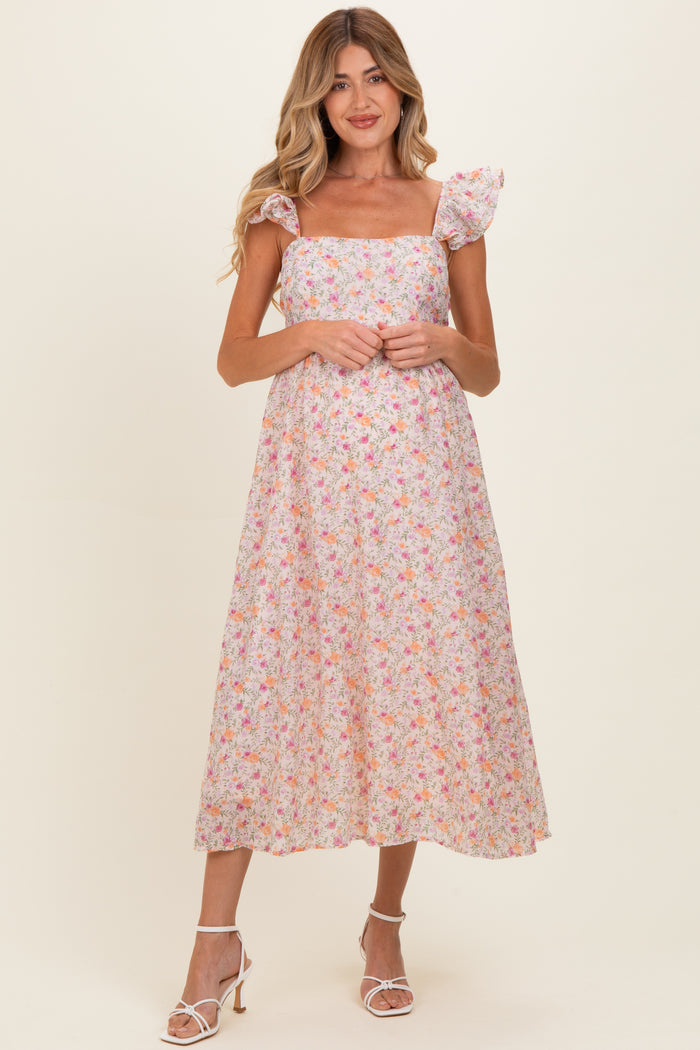 woman wearing a floral maternity dress with a square neckline and flutter sleeves, standing and smiling