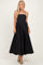 woman wearing a black strapless maxi dress with a flowy skirt and holding it slightly at the waist