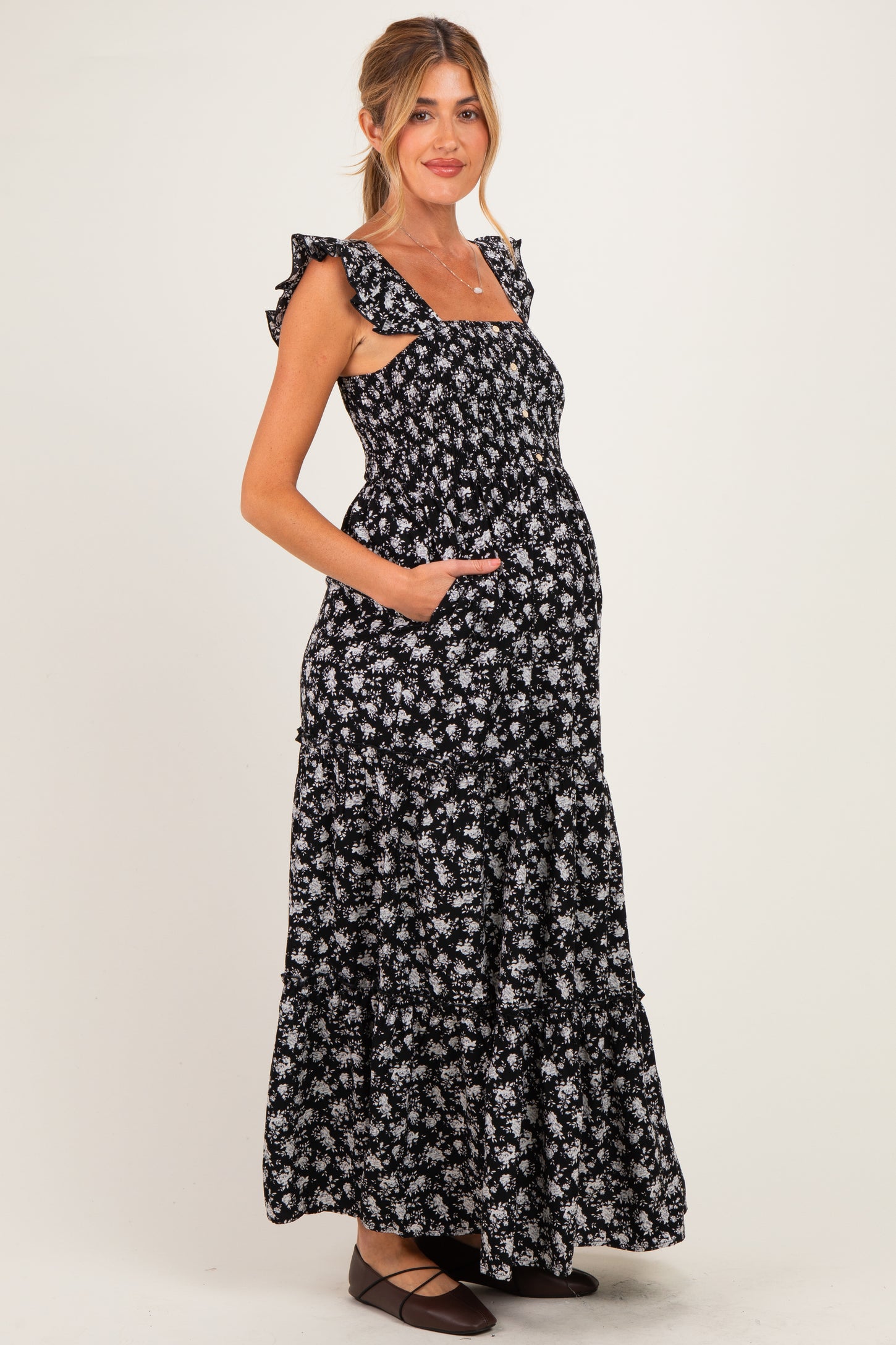 woman wearing a black floral maternity maxi dress with ruffle straps and pockets, showing her baby bump
