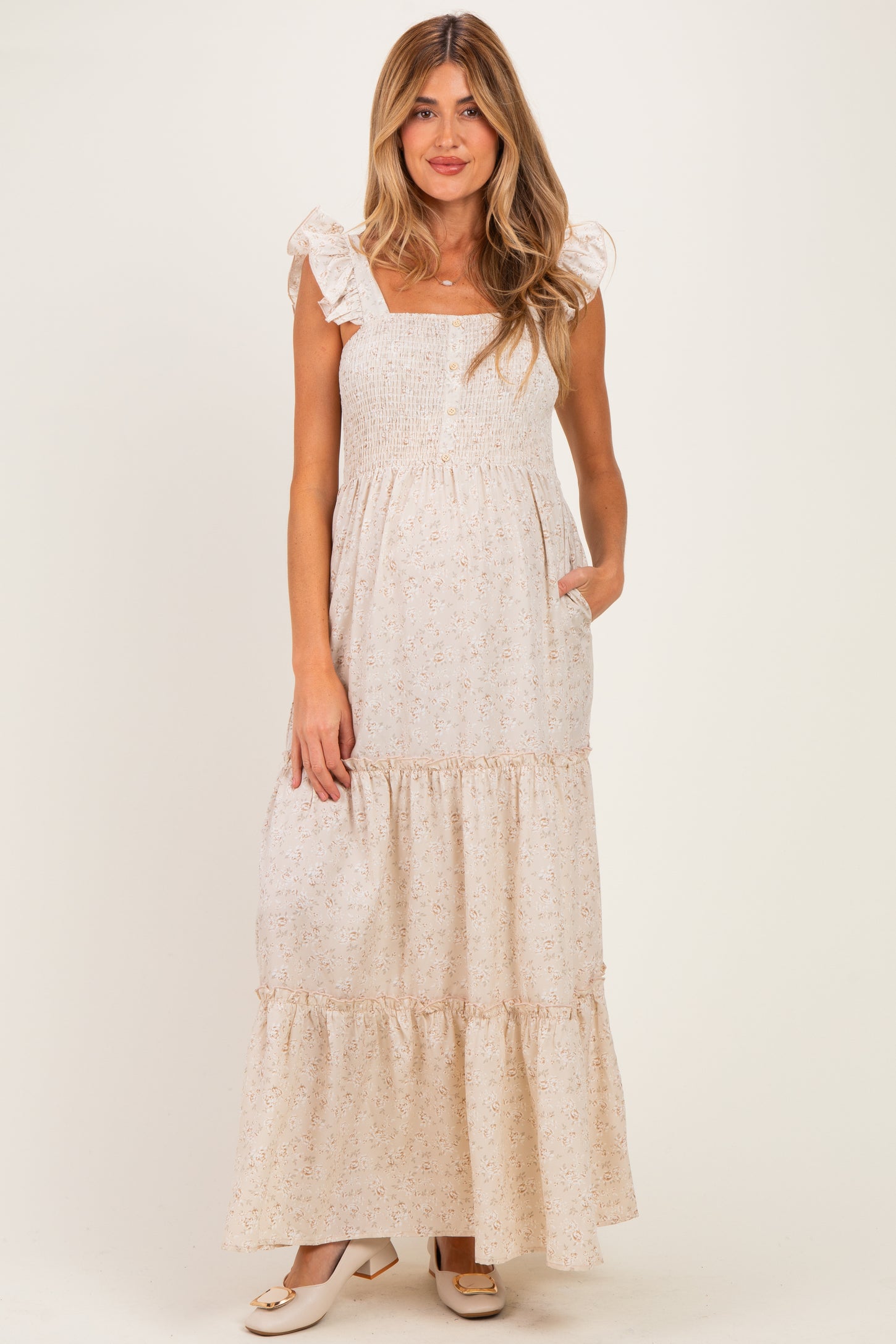 woman wearing a cream floral maternity maxi dress with ruffled straps and pockets, showing her baby bump