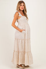 woman wearing a floral patterned maternity maxi dress with ruffled straps and a baby bump visible, posing with hands in pockets