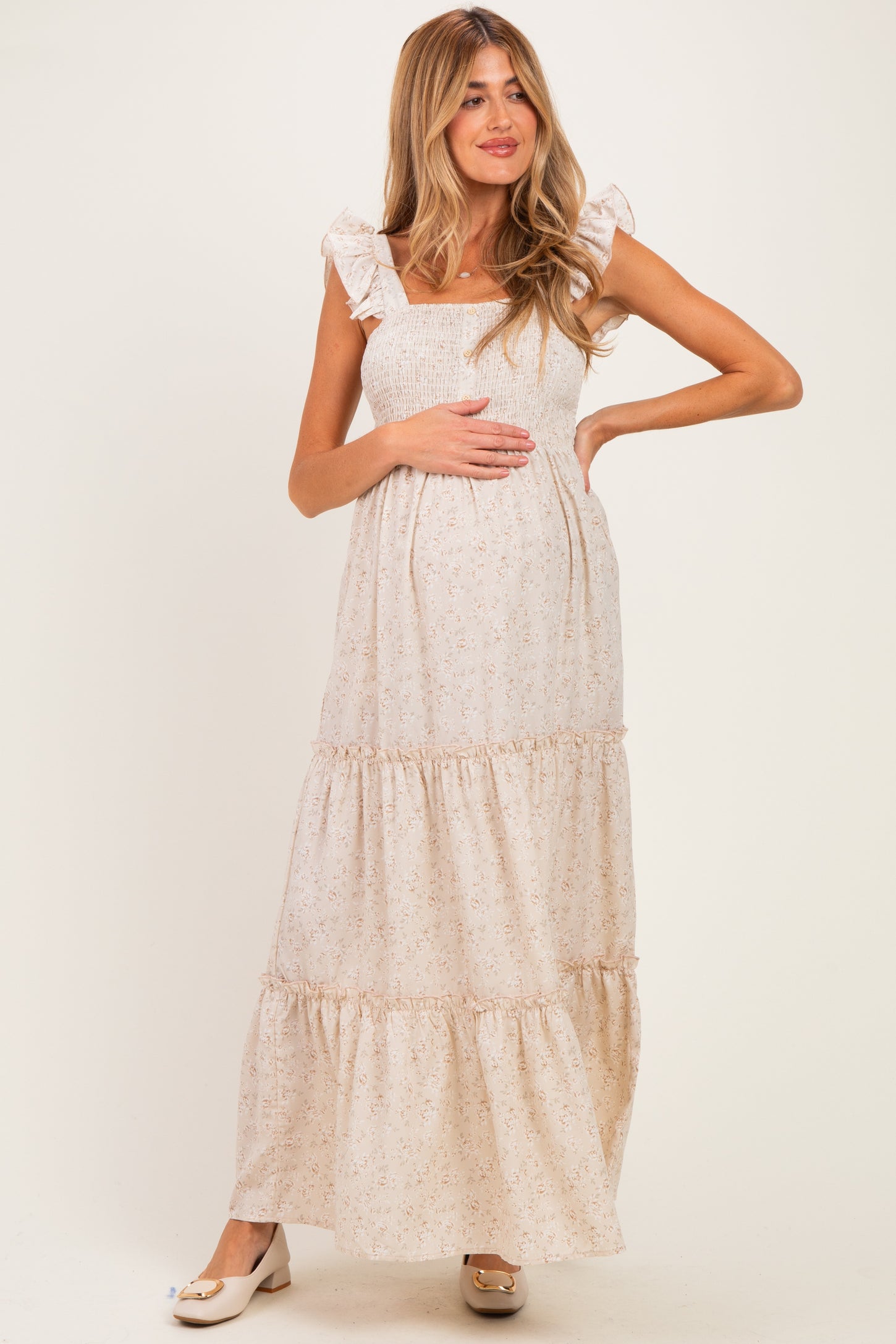 woman wearing a cream floral maternity maxi dress with ruffle straps and smocked bodice, holding her baby bump