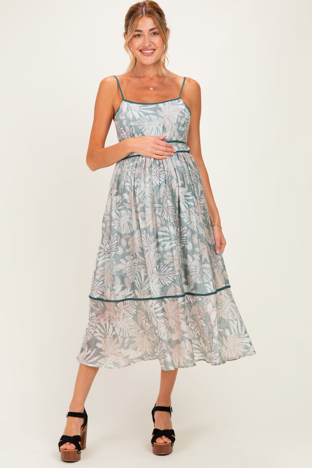 woman wearing a light blue floral maternity dress with thin straps and a flowing skirt, holding her baby bump