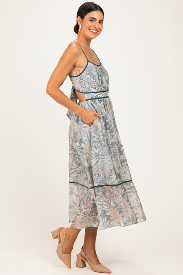 woman wearing a light green floral midi dress with pockets and a back tie detail, paired with beige heels