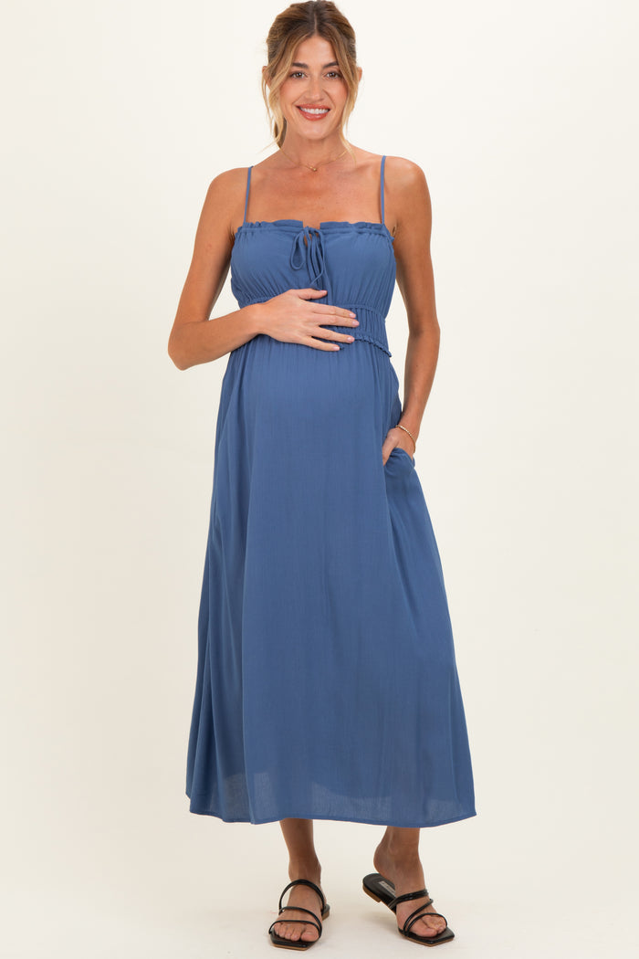 woman wearing a blue sleeveless maternity maxi dress with a tie front and pockets, showcasing her baby bump