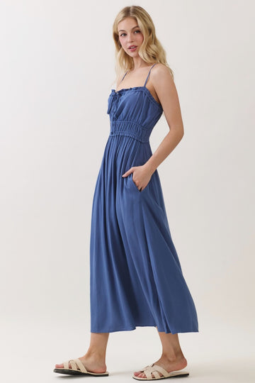 woman wearing a blue maxi dress with smocked bodice and pockets, standing in a neutral background