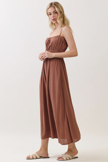 woman wearing a brown maxi dress with a smocked bodice and adjustable straps, paired with slip-on sandals