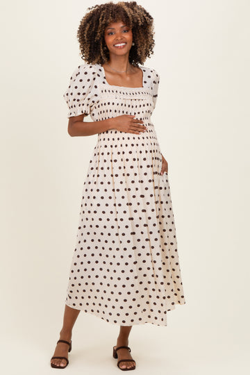woman wearing a cream maternity dress with brown polka dots, puff sleeves, and a shirred bodice, showcasing her baby bump