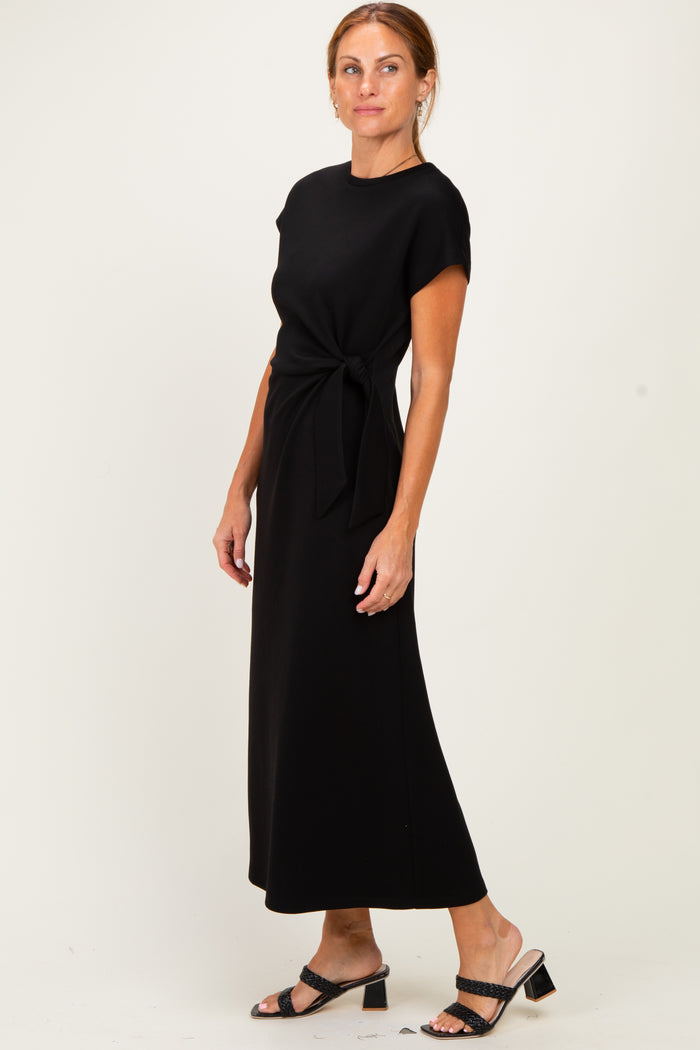 woman wearing a black cap sleeve maxi dress with a tie detail at the waist and black heeled sandals