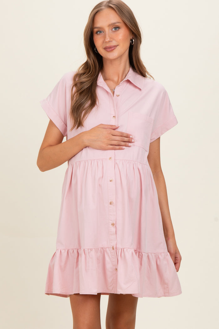 woman wearing a light pink maternity shirt dress with short sleeves and ruffle hem, holding her baby bump