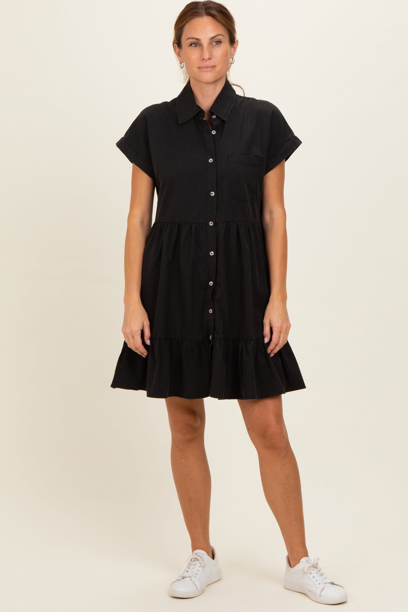 woman wearing a black short sleeve button-up dress with a tiered skirt and side pockets, styled with white sneakers