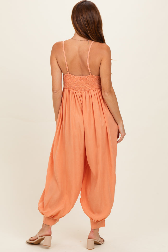 woman wearing an orange smocked-back jumpsuit with wide leg and spaghetti straps, viewed from the back