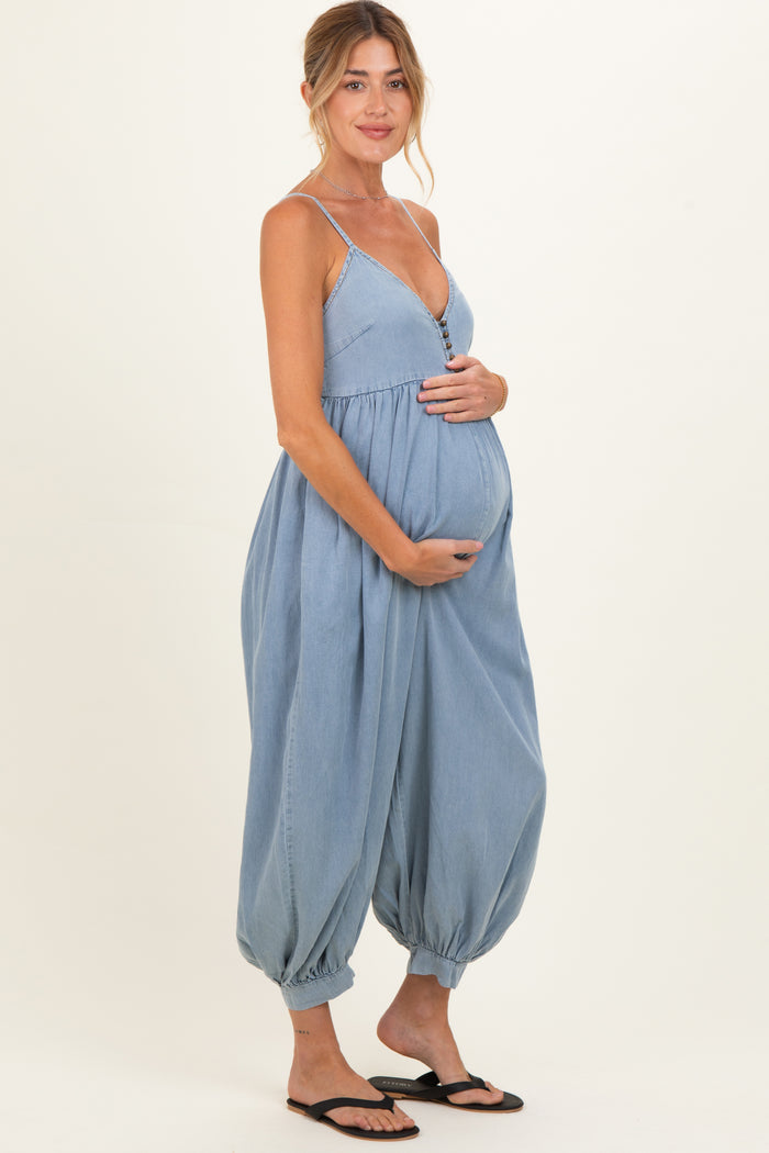 woman wearing a light blue maternity jumpsuit with button details and holding her baby bump
